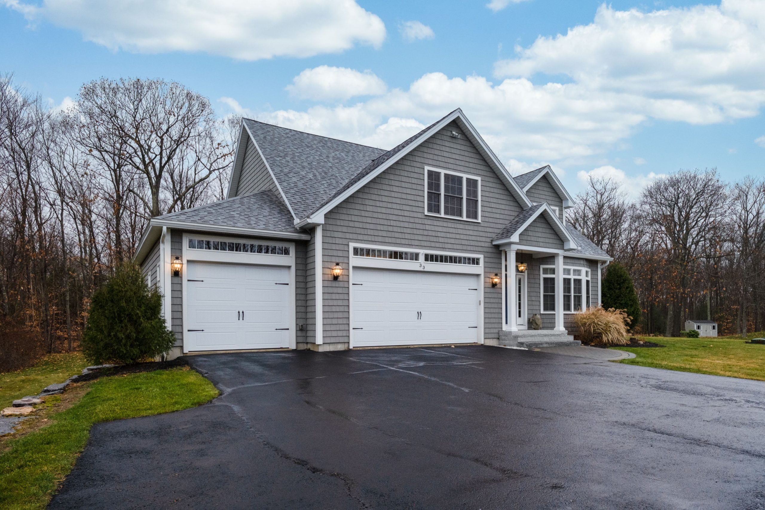 Cozy suburban charm: A modern grey home with a welcoming porch and a spacious double garage, nestled against a backdrop of autumn woods.